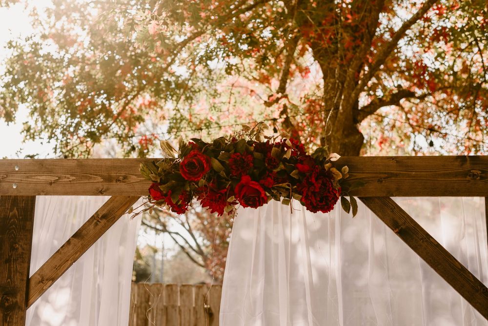 Red roses and white fabric decorate a wooden wedding arch against an autumn backdrop.
