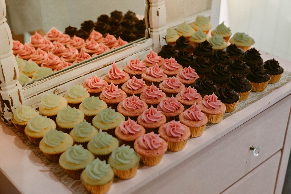 Colorful array of cupcakes with pink, mint green, and chocolate frosting displayed at a wedding.