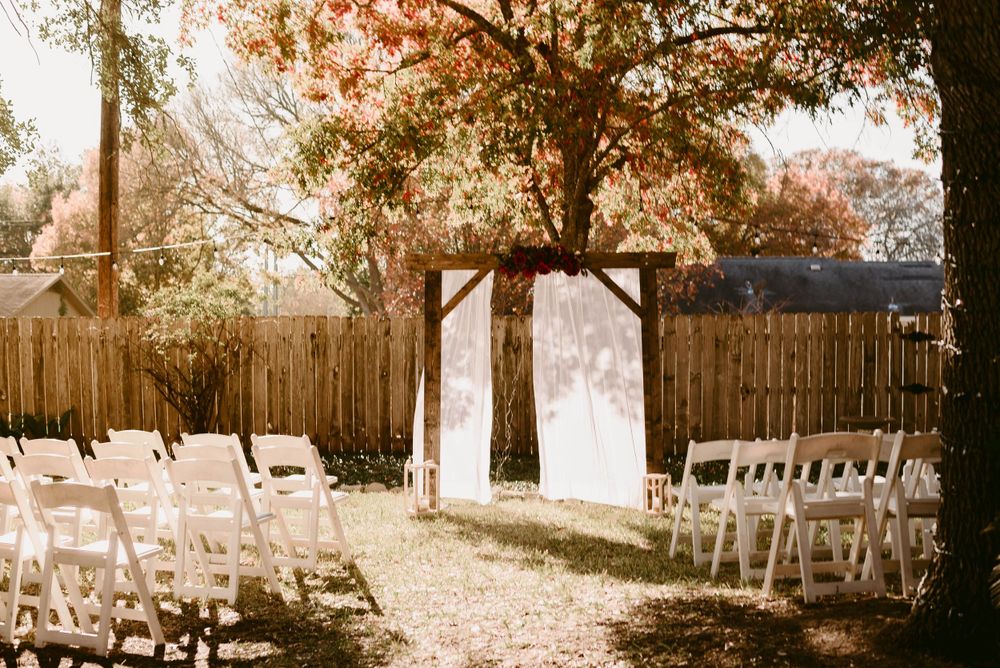 White chairs lined up for an outdoor wedding ceremony with a wooden arch and privacy fence.