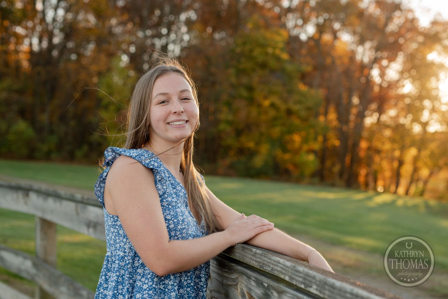 A joyful pose against a wooden fence with autumn colors glowing in the background.
