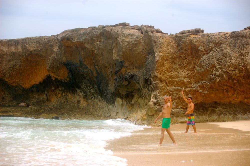People enjoy the beach near dramatic rocky cliffs and crashing waves.