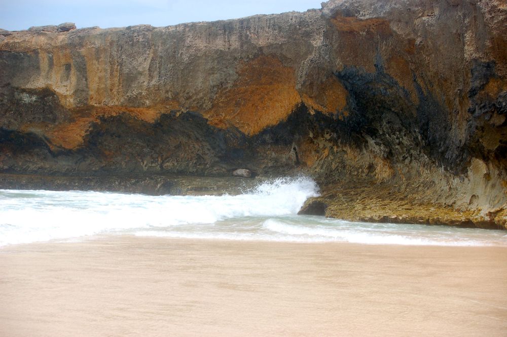 Dramatic rocky cliffs tower over a sandy beach with crashing waves.