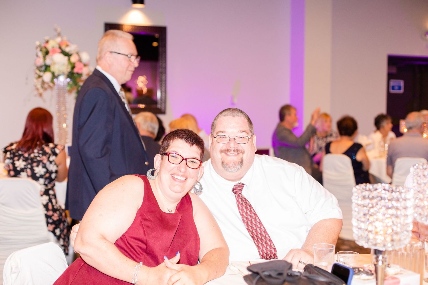 Wedding reception venue with purple lighting and guests seated at round tables.