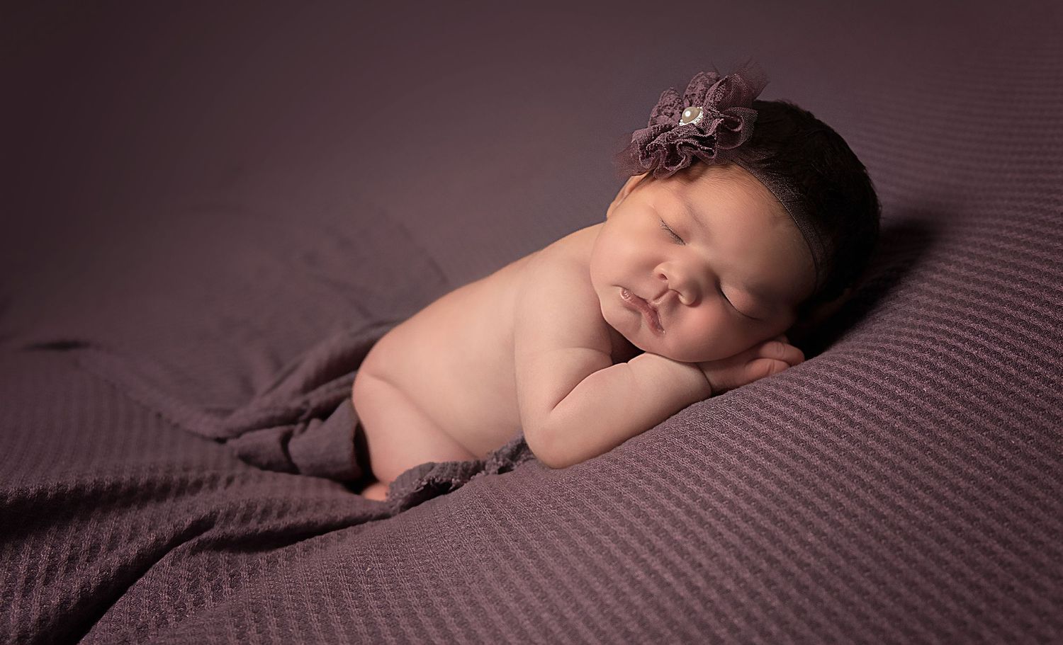 Peaceful sleeping newborn baby wrapped in purple fabric during studio photography session.