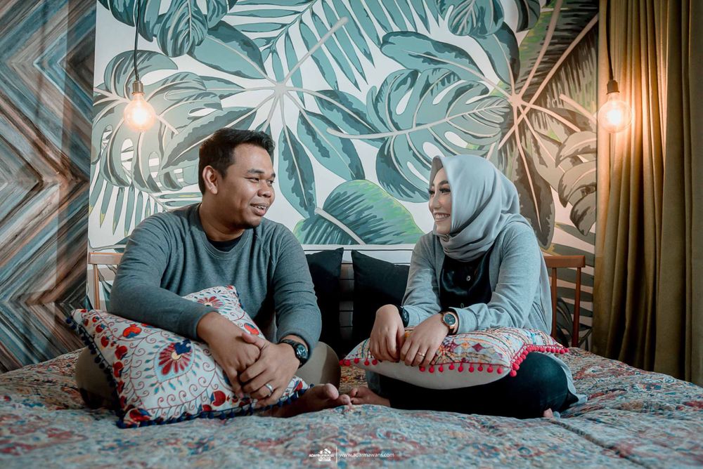 Couple relaxing on bed with tropical leaf wallpaper and decorative pillows.