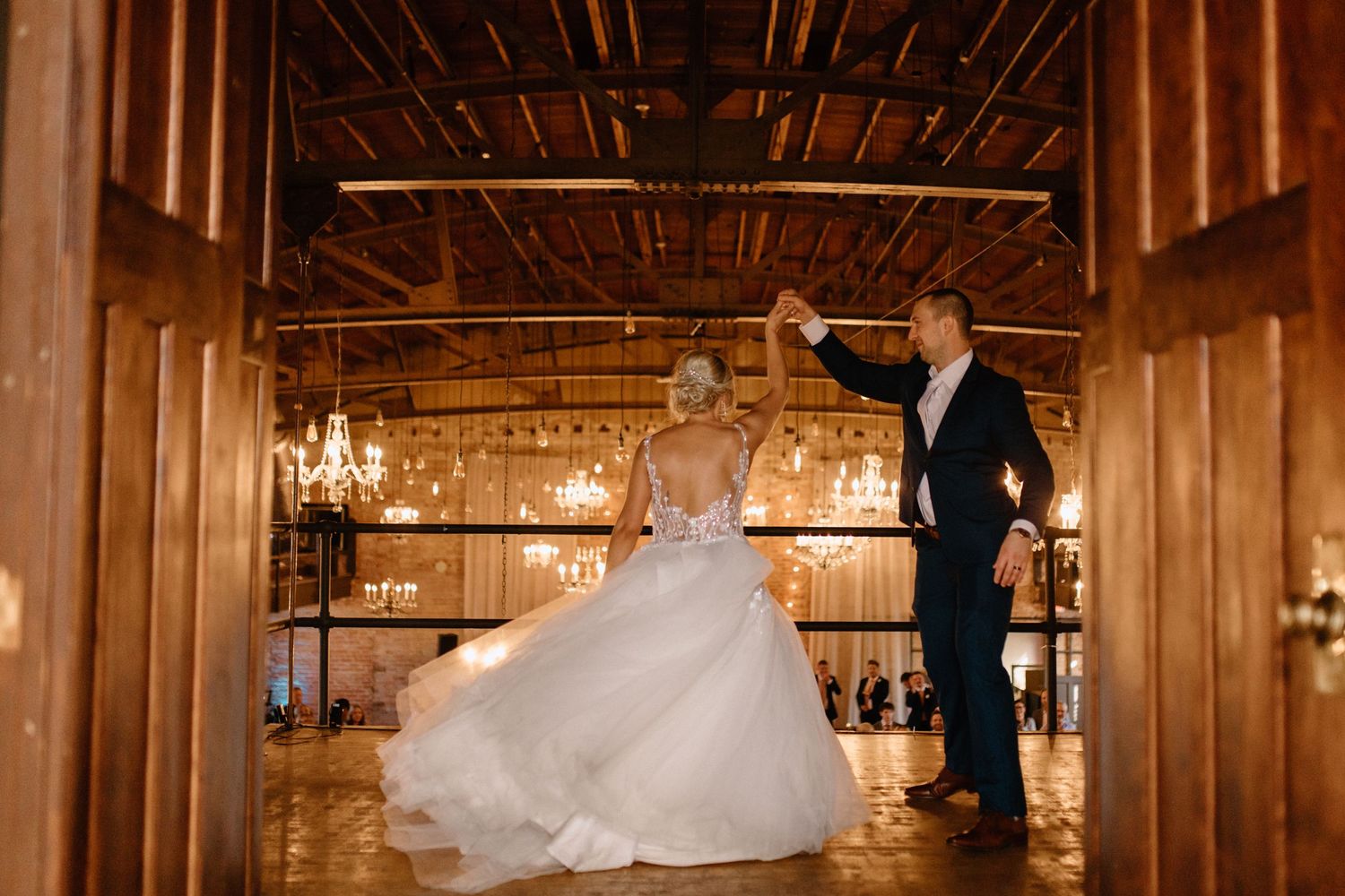 A couple dances in an elegant rustic venue with wooden beams and chandeliers.
