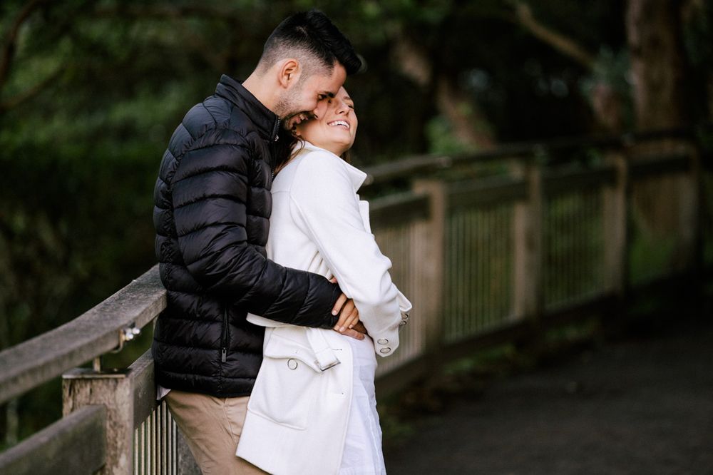 Intimate moment captured between two people in a park with trees in the background.