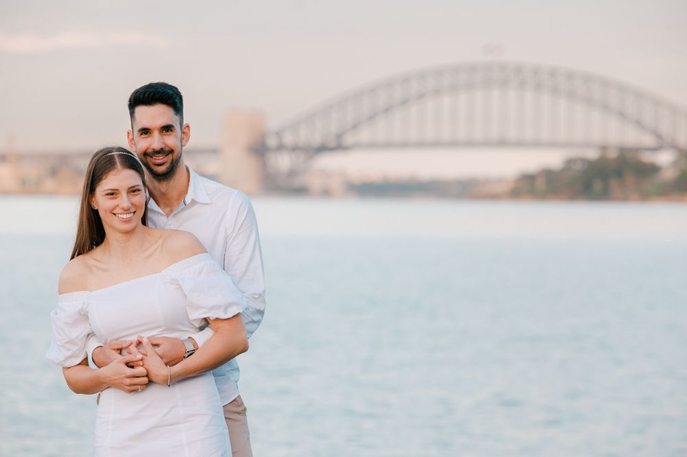 Couple in white outfits sharing romantic moment by Sydney Harbour.