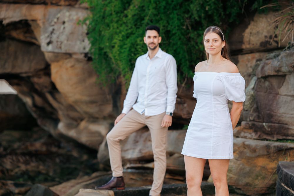Couple posing against rocky cliffside backdrop with green foliage.
