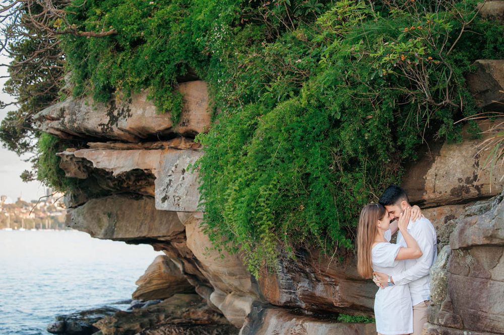 Engagement photos at rocky coastal location with lush greenery.