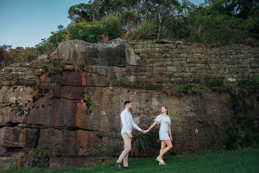Couple enjoys romantic moment against scenic stone wall backdrop with trees.