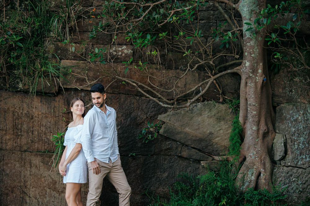 Couple walks hand in hand along historic stone wall pathway during outdoor photo session.