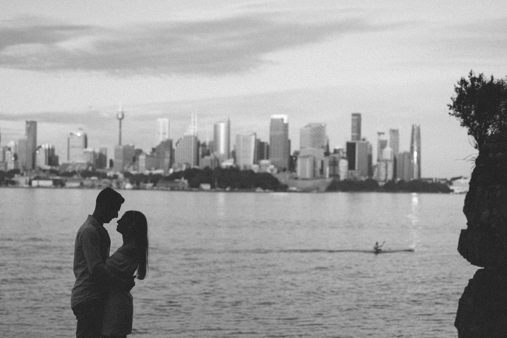 Silhouetted couple against city skyline and waterfront during sunset.