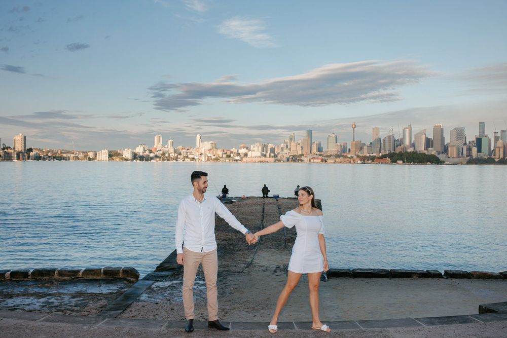 Couple poses playfully with downtown skyline and harbor waters in background.