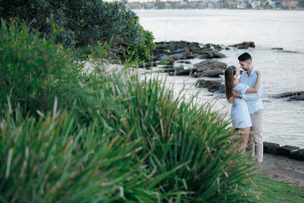 Couple strolls along waterfront path with harbor views during photo session.