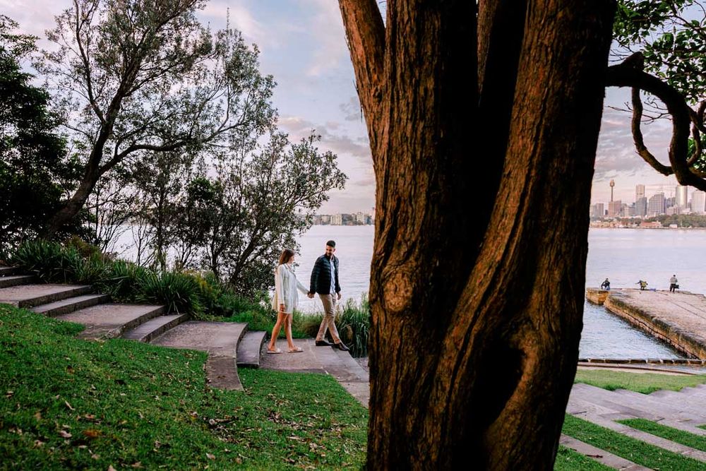Scenic waterfront path with trees and city skyline in the distance.