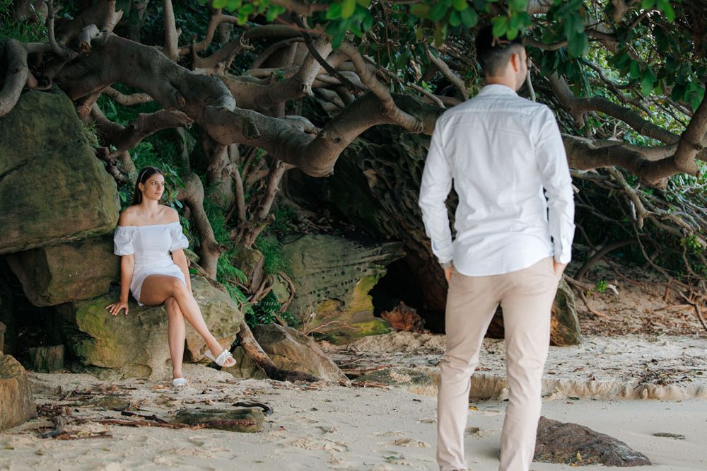 Romantic beachside moment under overhanging trees and rocks.