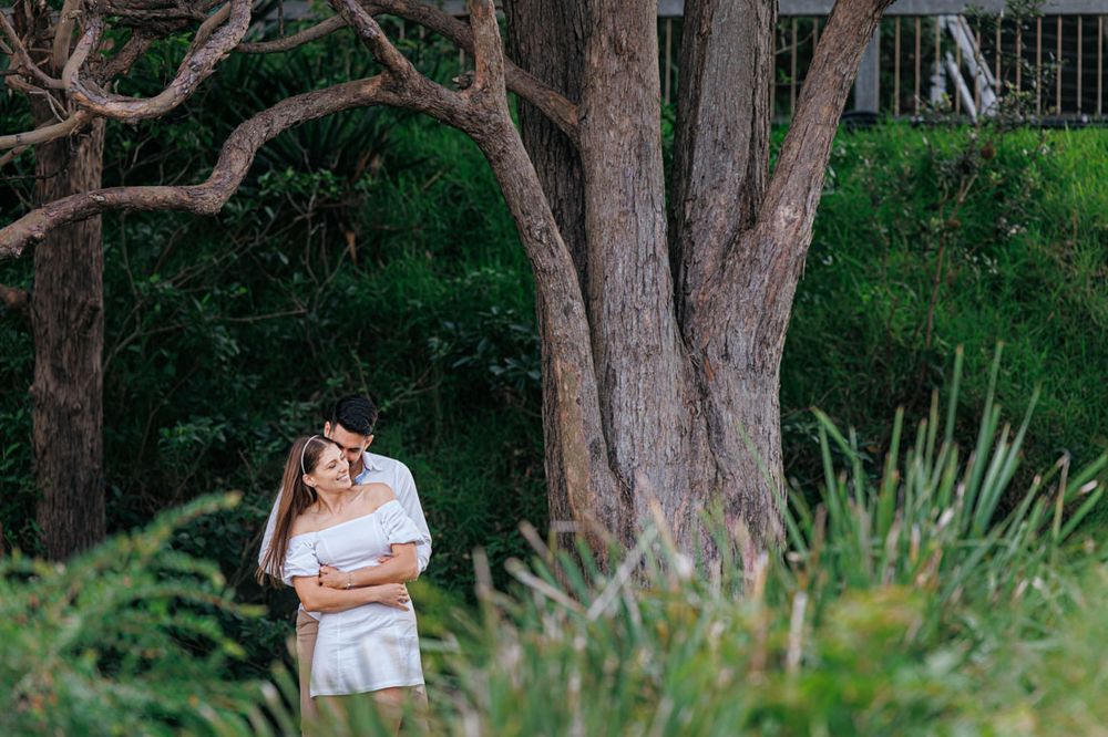 A couple sits beneath large tree branches in a park setting.