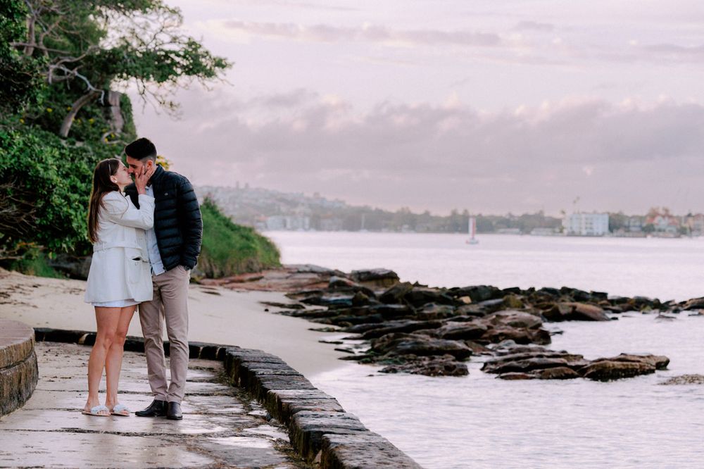Scenic coastal path with rocky shoreline and city buildings in the background.