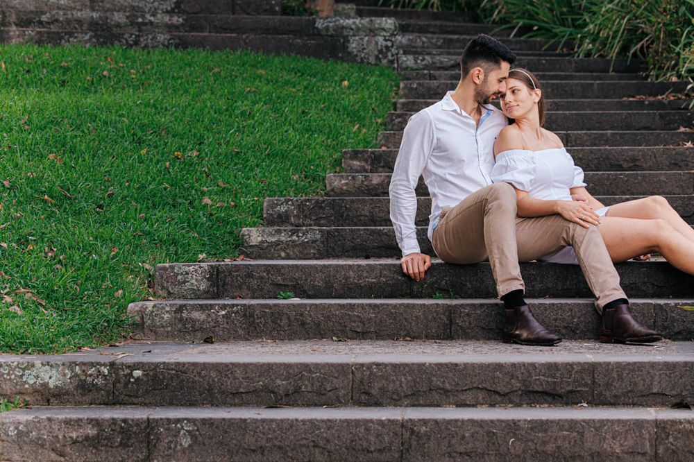 A couple relaxes on stone steps surrounded by green grass in a park.