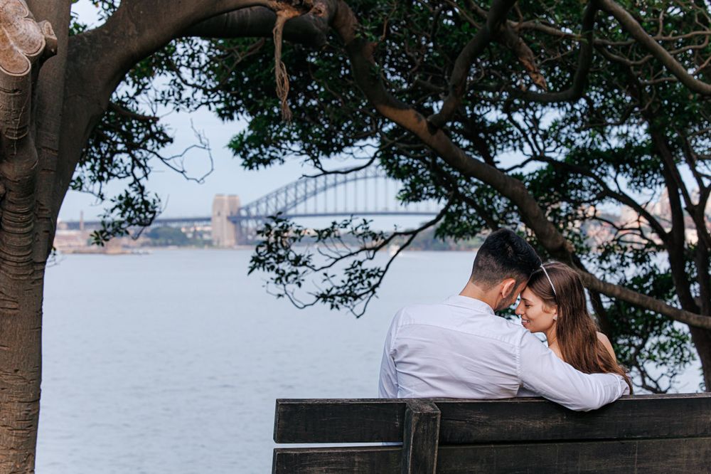 couple hugging on the bench with Sydney Harbour Bridge in the background