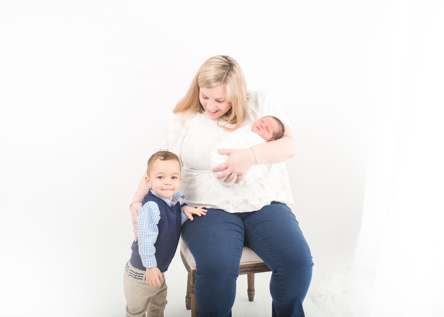 two year old smiling with his mom and newborn baby boy for an all white theme newborn studio session in houston