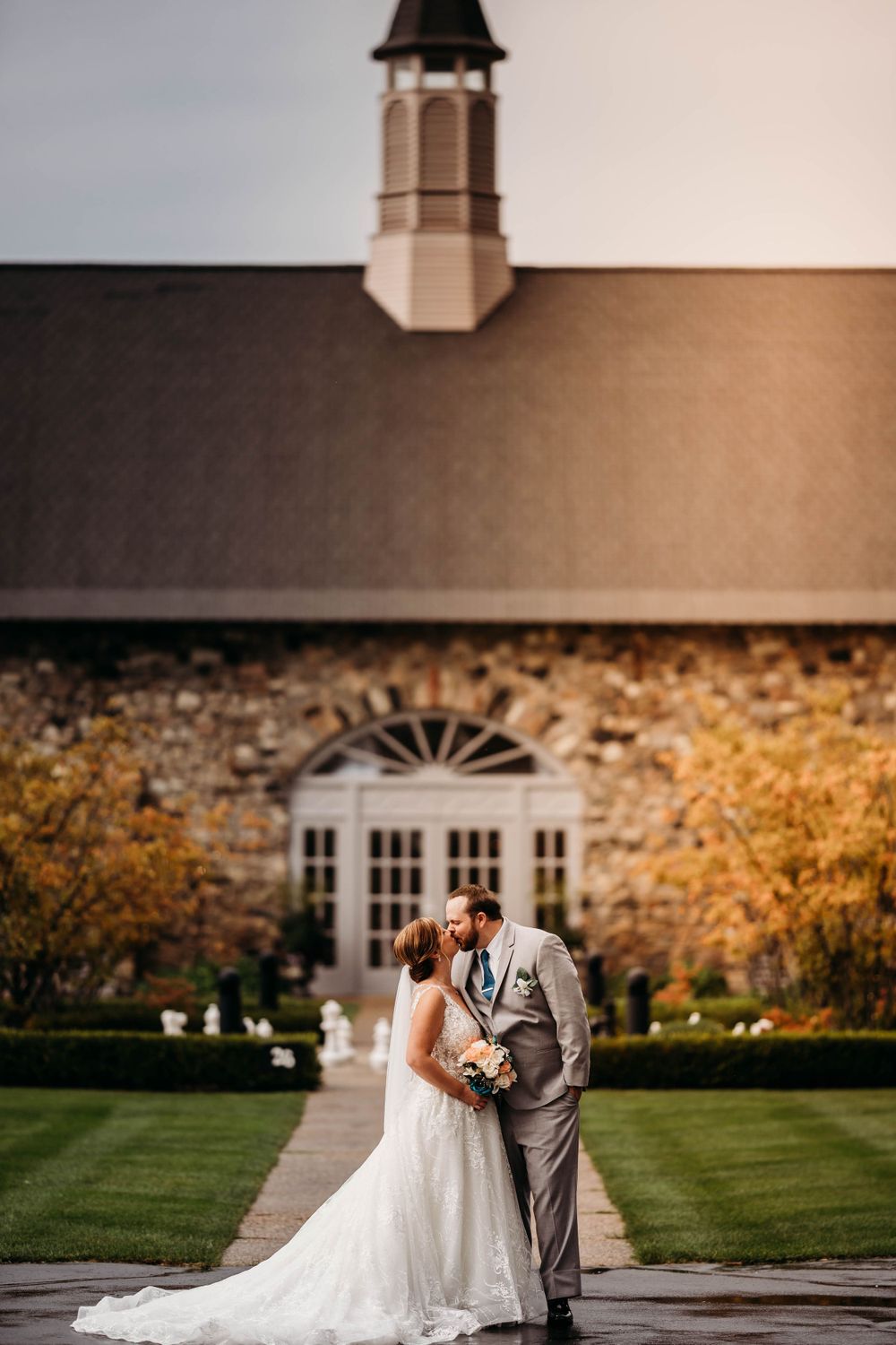 Wedding couple embraces on stone patio in front of elegant venue with white windows.