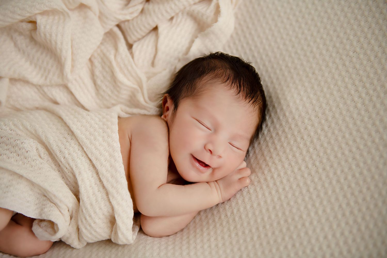 Sleeping newborn baby wrapped in cream blanket on textured background.