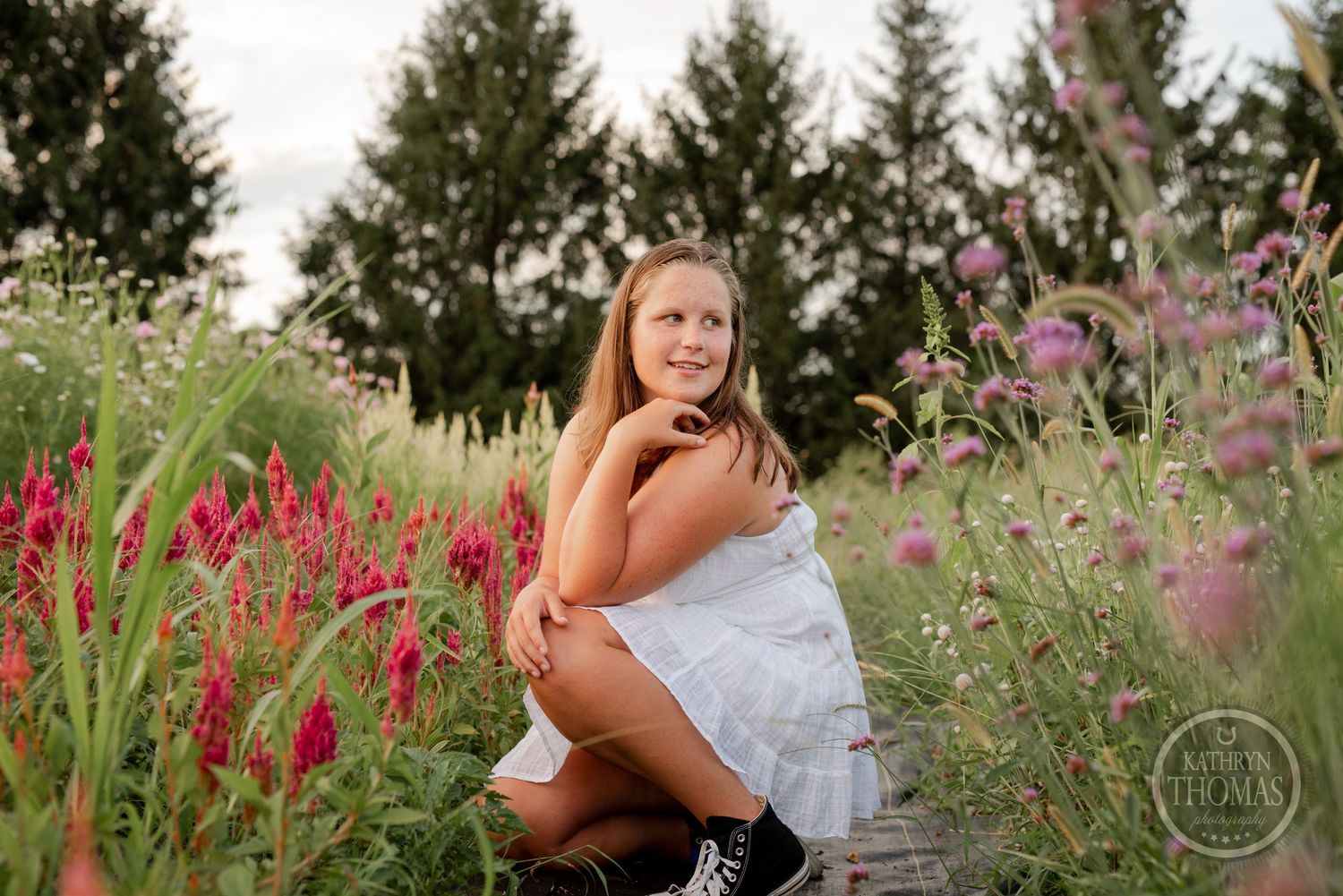 A dreamy summer portrait in a garden with red and purple wildflowers against evergreen trees.