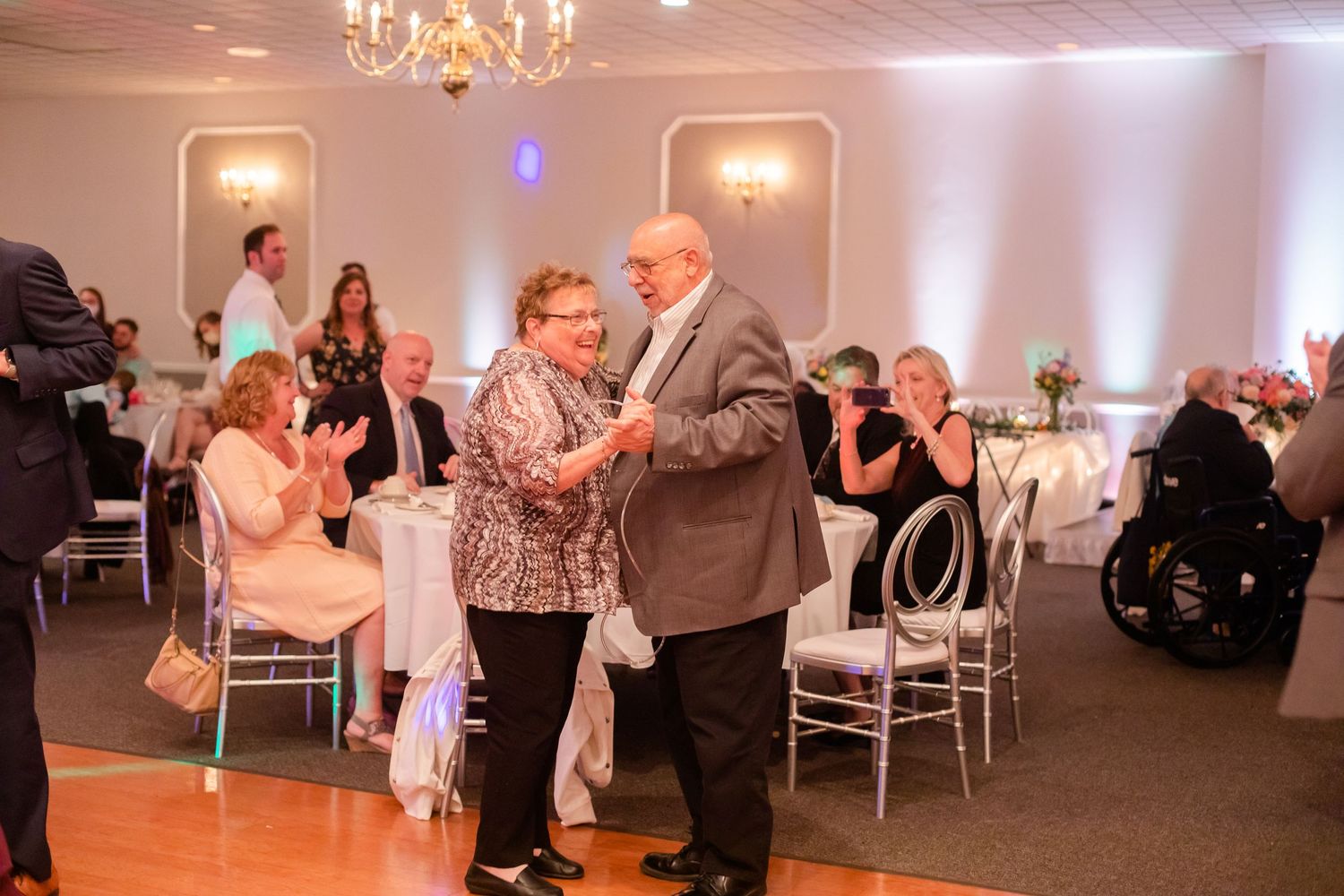 Couples dancing together in an elegant ballroom with chandeliers and soft lighting.