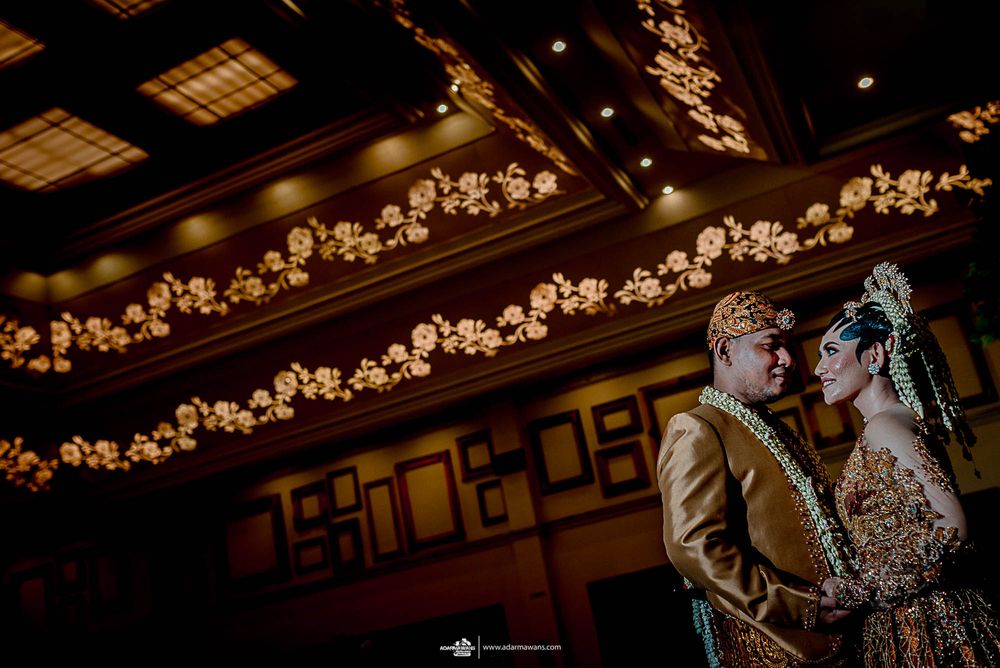 Dramatic indoor wedding portrait with warm overhead lighting and string lights.