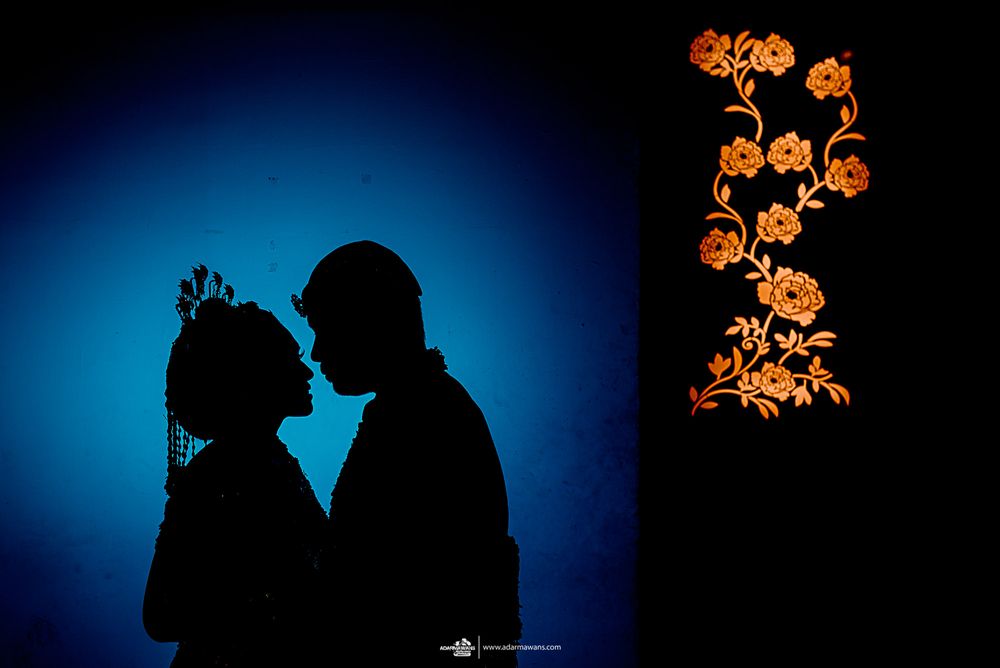 Silhouette of wedding couple against blue backdrop with orange floral decorative elements.