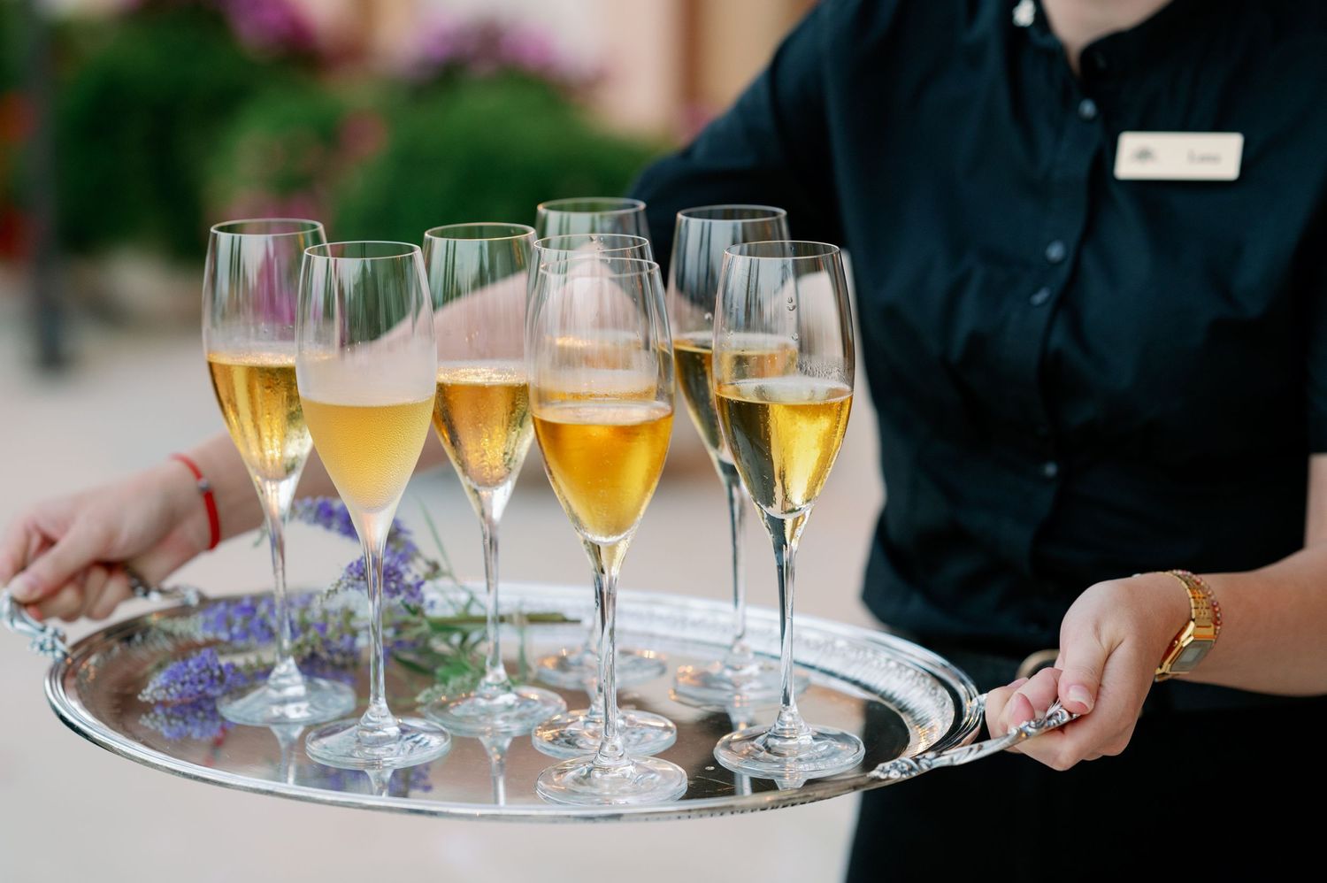 Server carries tray of champagne flutes filled with golden bubbling wine.