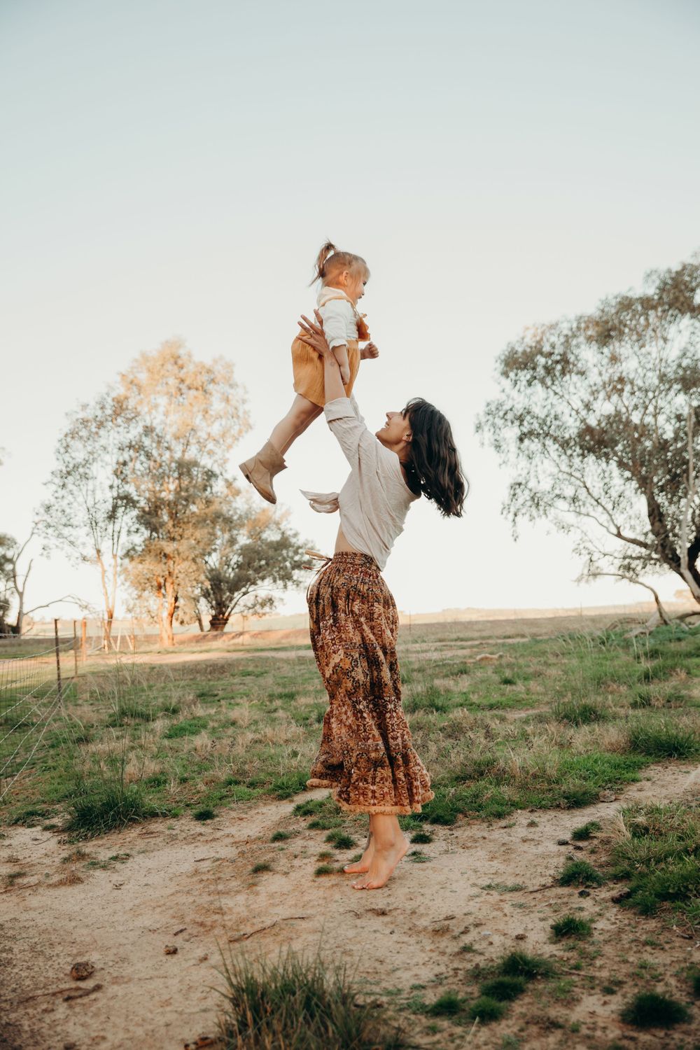 Mother lifting her toddler high in the air in a sunny rural Australian field.