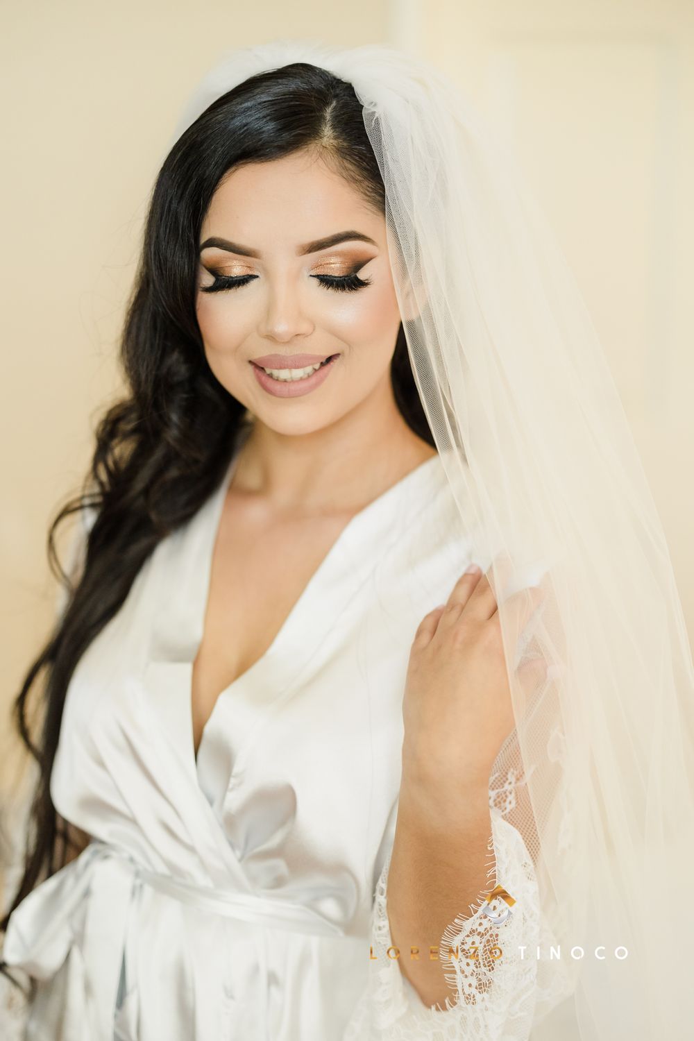 Radiant bride wearing veil and silk robe smiles during wedding morning preparations.