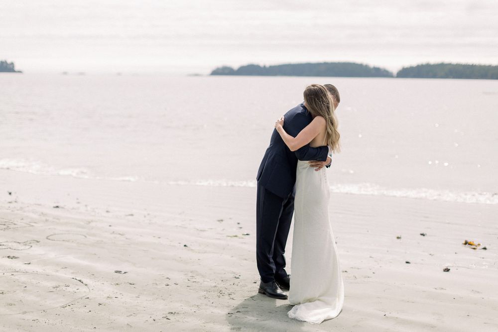 Bride and groom sharing tender embrace on wide sandy beach during intimate elopement ceremony.