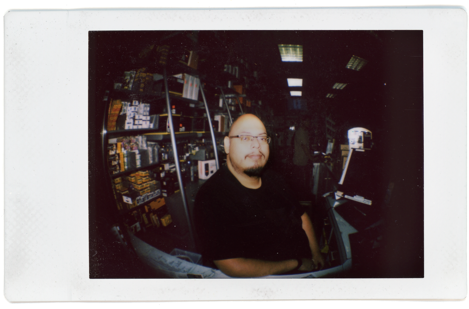 Man with glasses posing inside a store captured on Instax film with a fisheye lens effect.