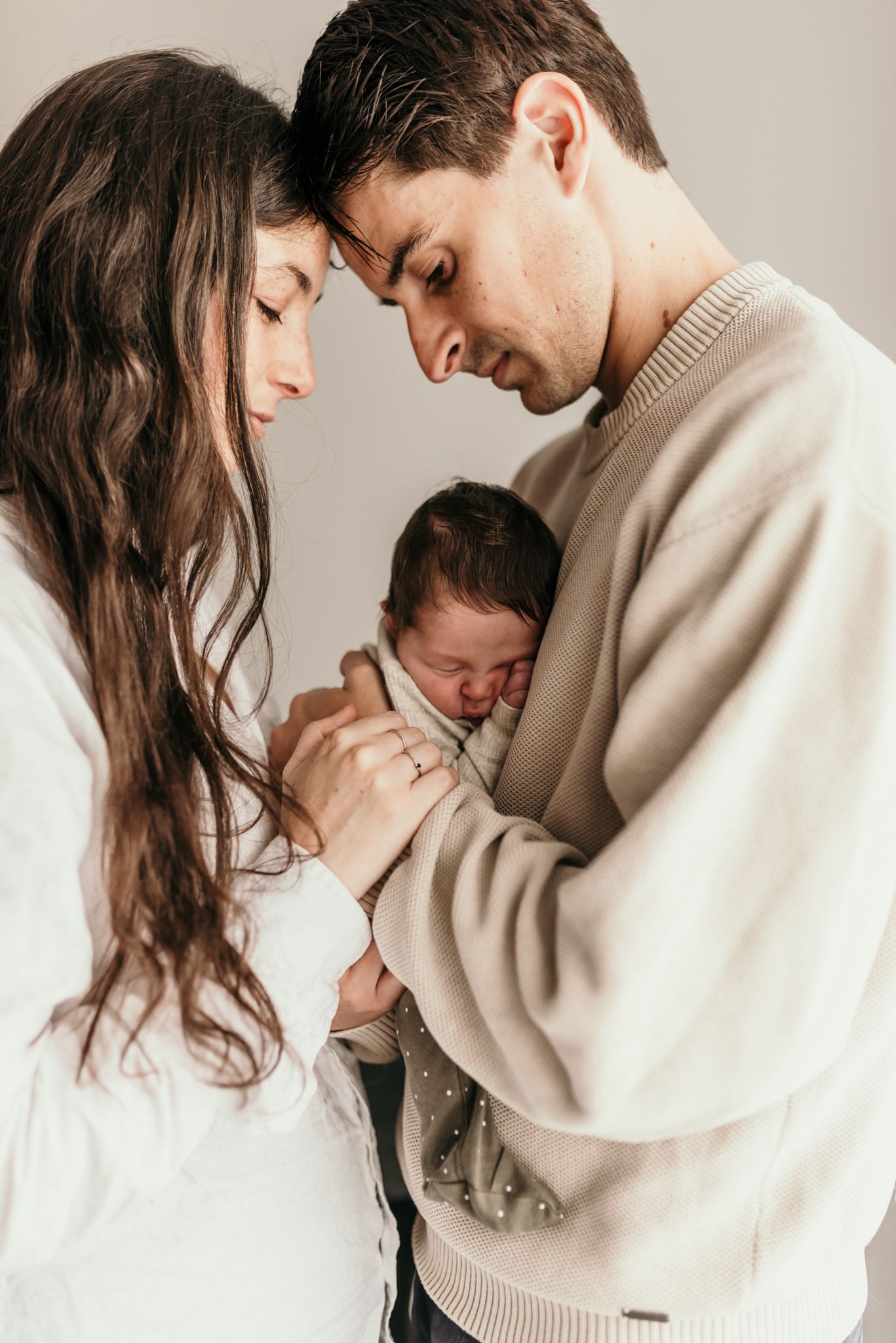 Intimate family moment with sleeping newborn baby held between two loving adults.