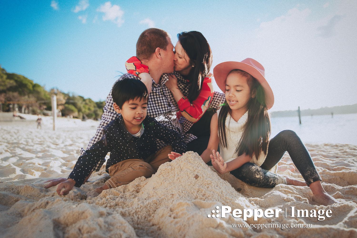 A loving family of four shares a kiss and plays in the sand on a sunny beach.