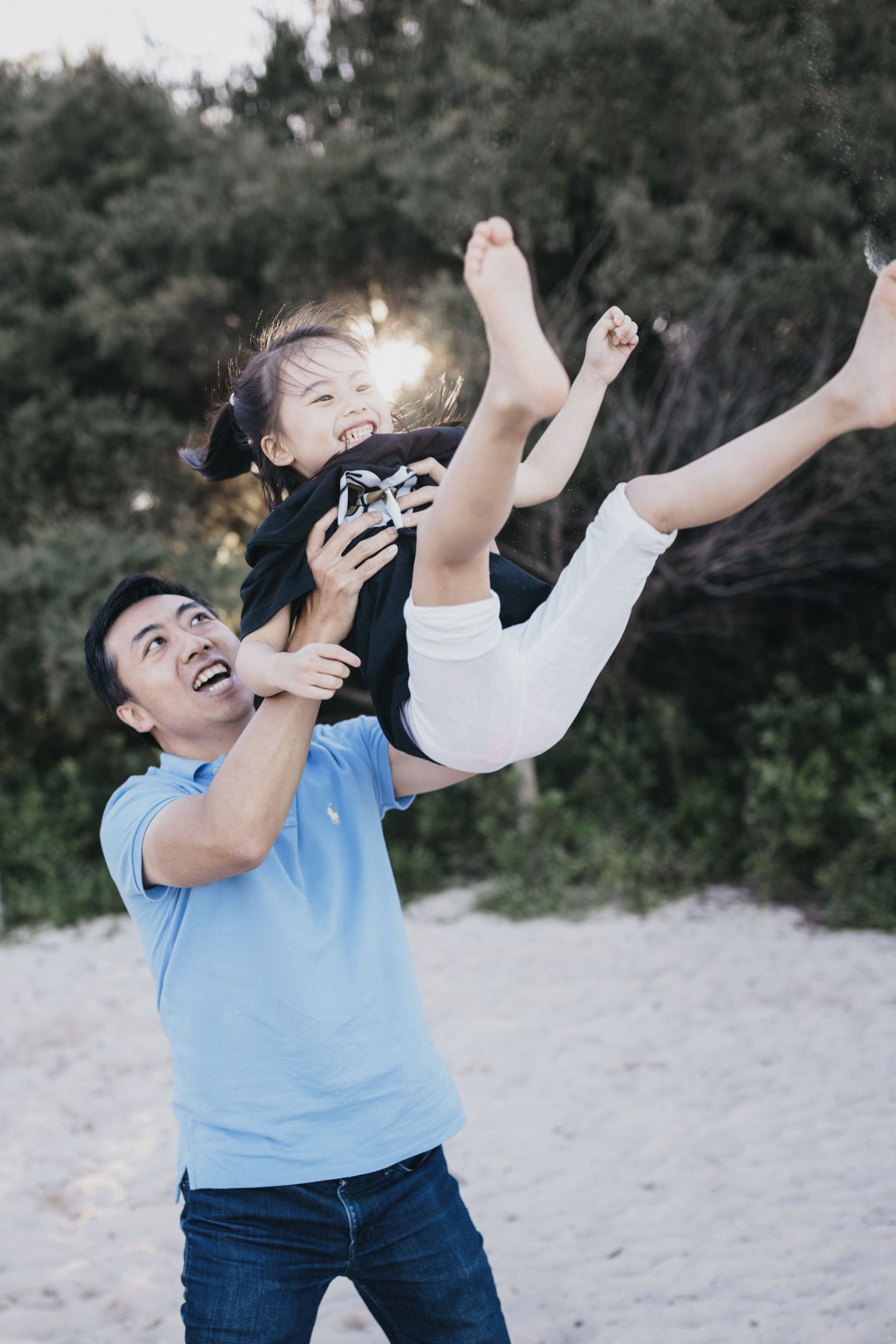 A cheerful father lifts his young daughter high in the air on a sandy beach at sunset.