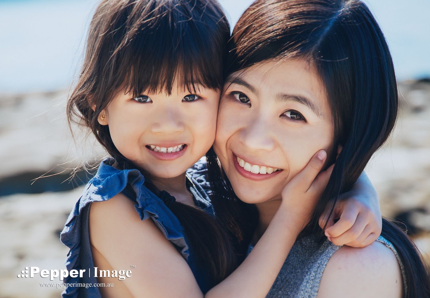 Mother and young daughter smiling closely together in a warm outdoor portrait.