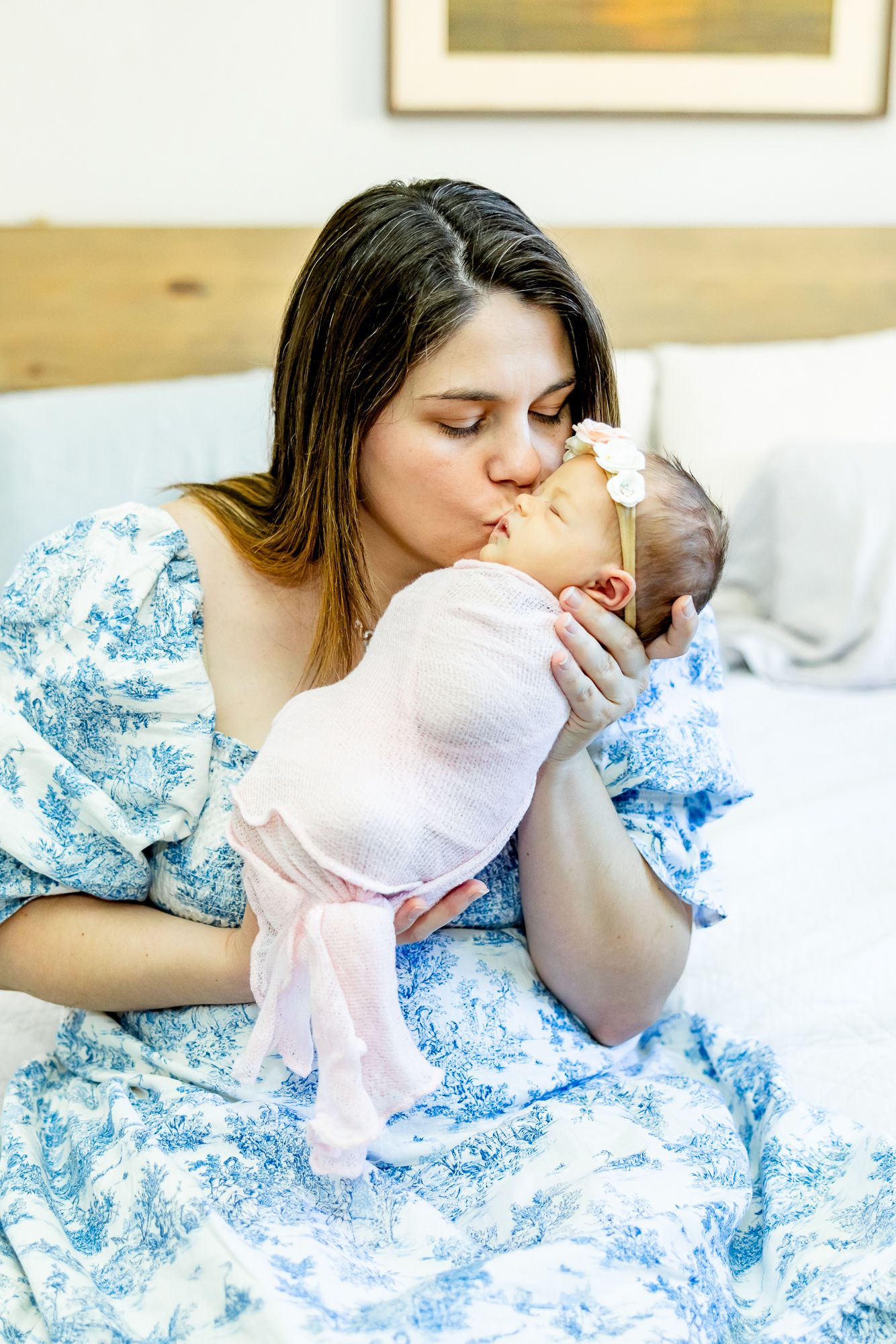 Mom sits holding up her new baby girl and kisses her during lifestyle newborn photos in Colorado Springs.