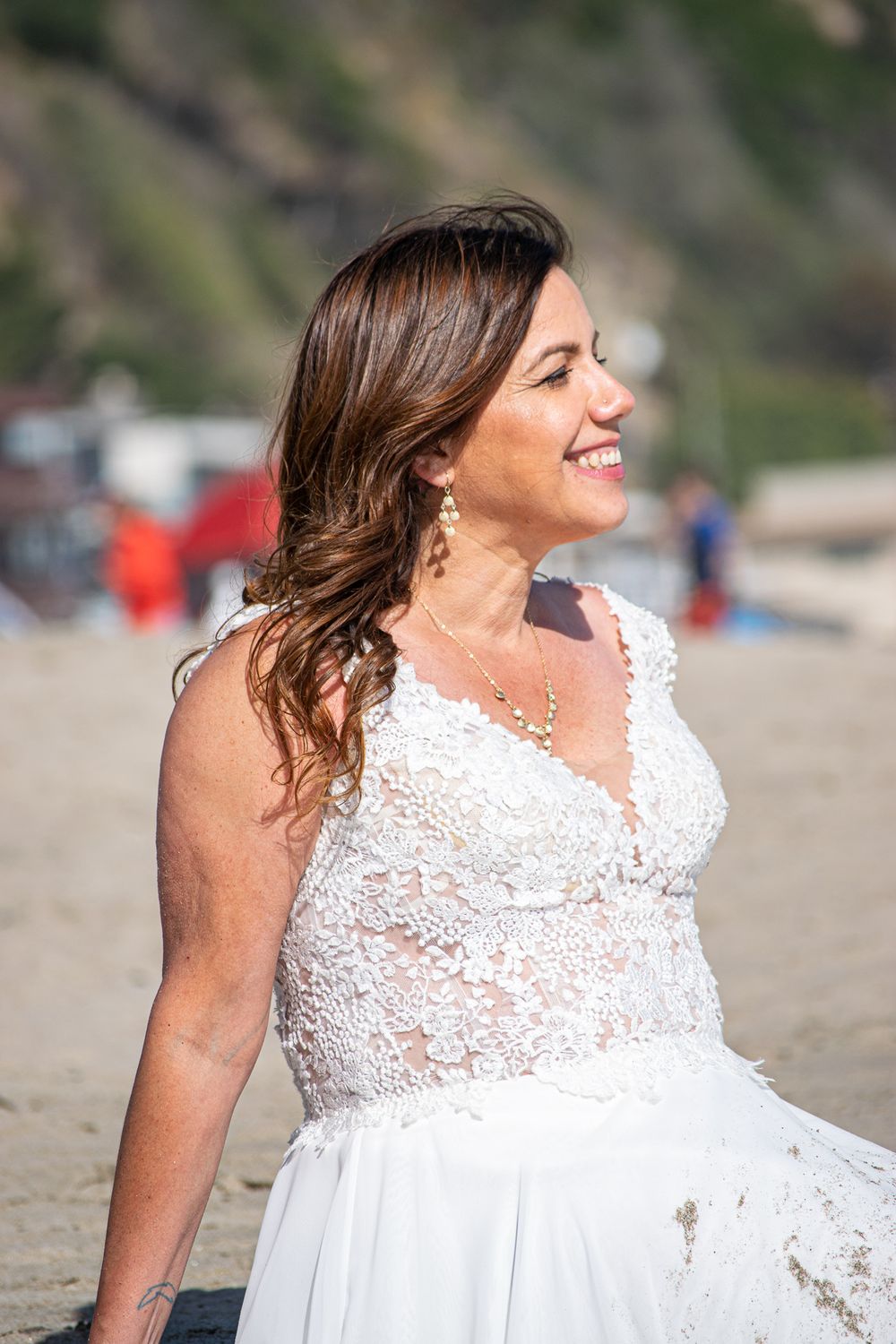 Woman Smiling in wedding dress sitting in the sand on a sunny California beach