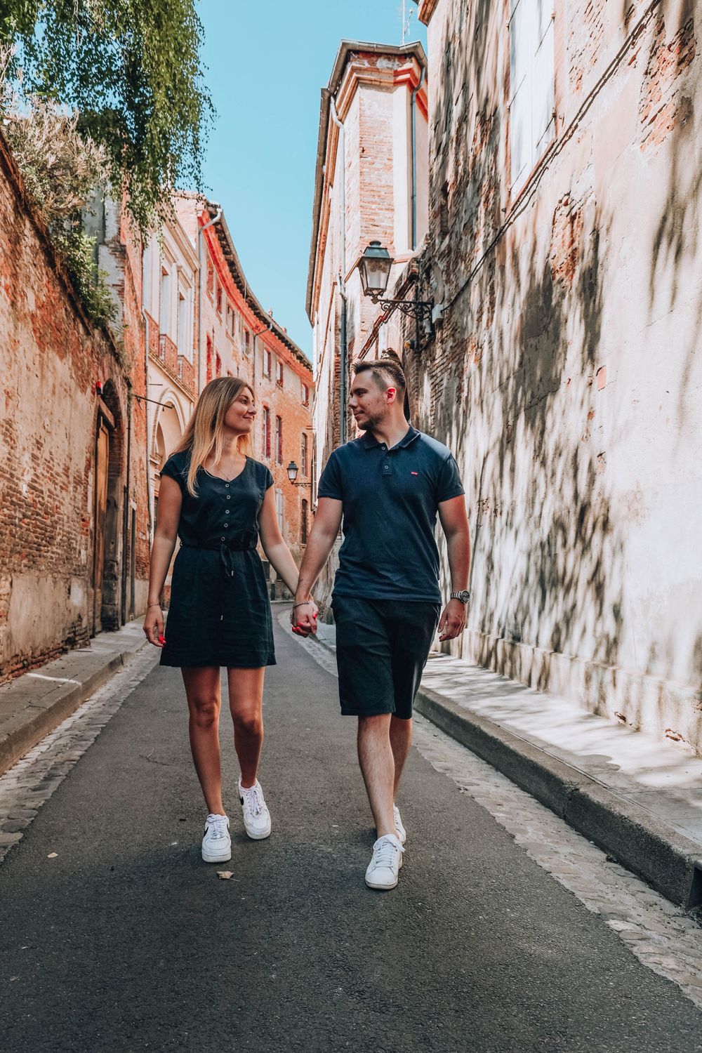 Couple holds hands while walking down a charming European alleyway with historic architecture.