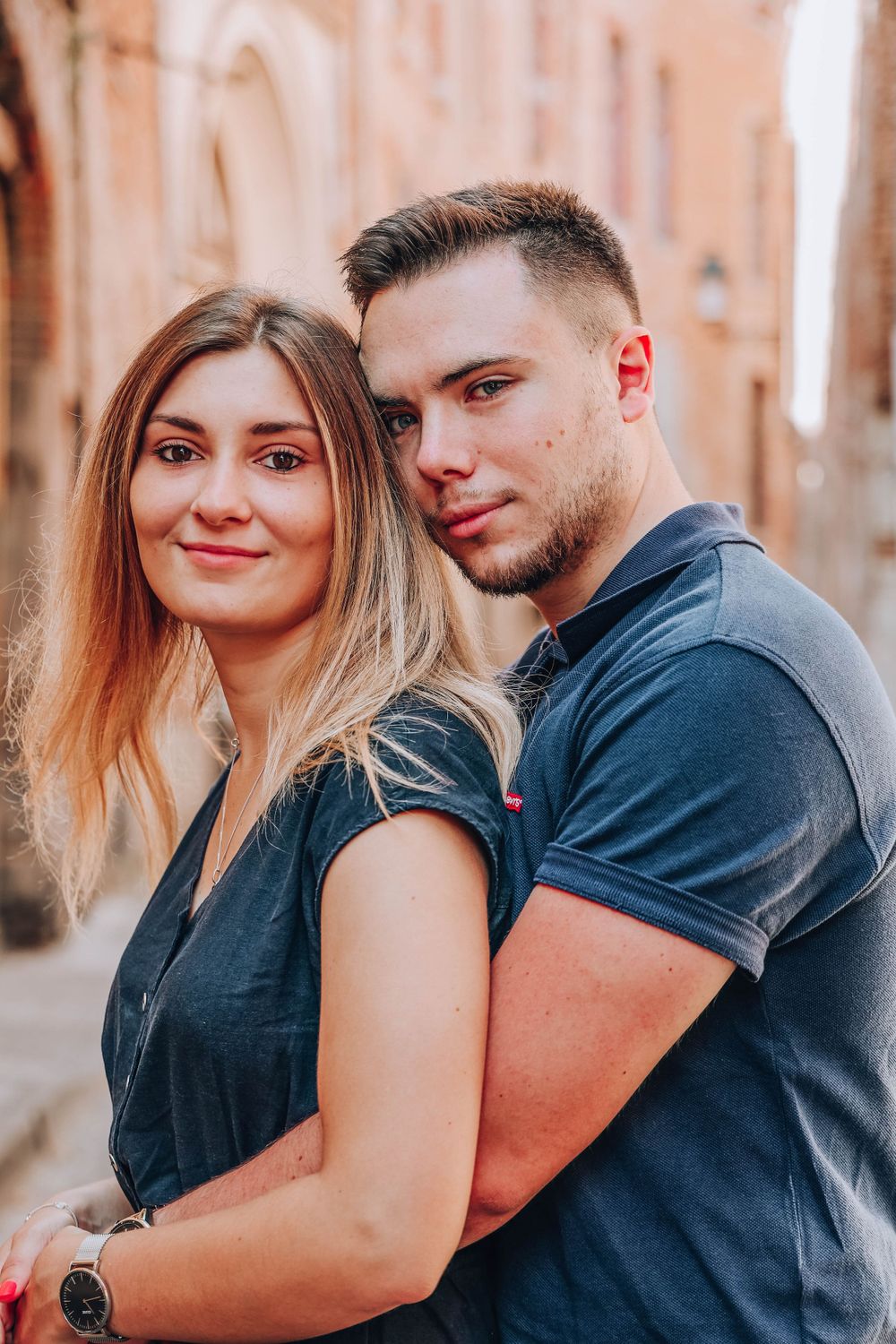 Romantic couple poses together against a soft blurred background in warm lighting.