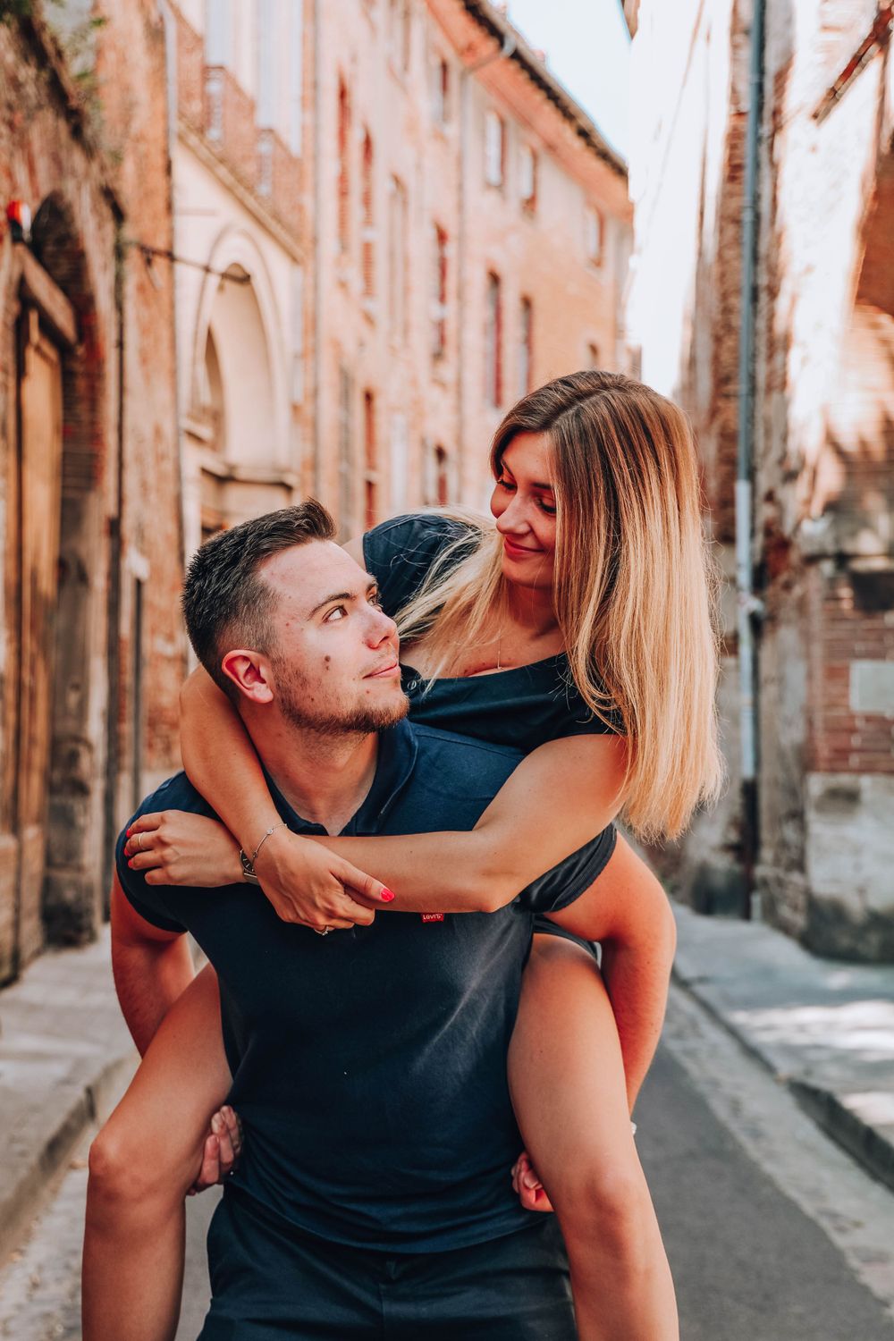 Playful piggyback ride along charming European alleyway with terracotta walls.