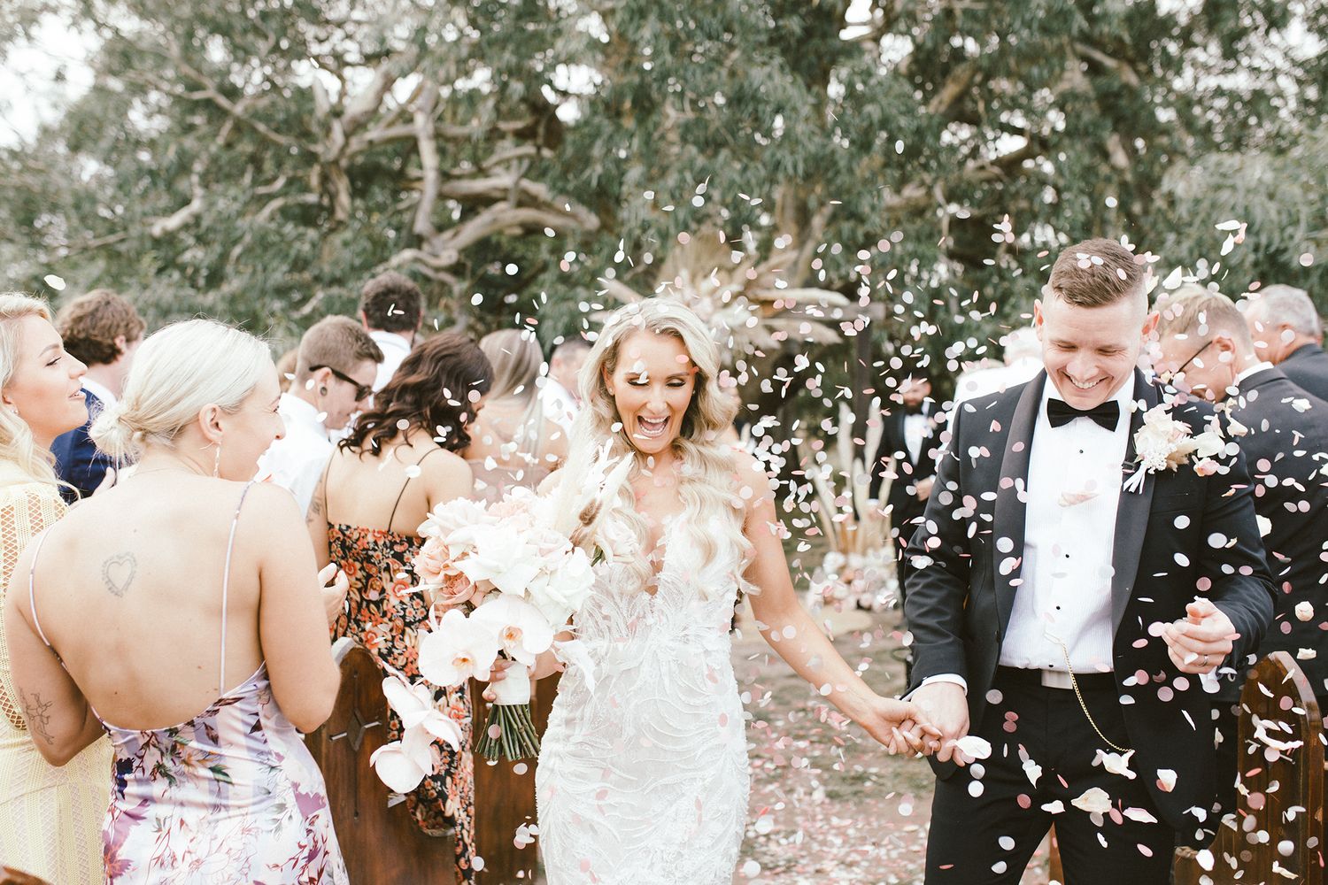 Wedding party showered with white confetti during outdoor garden celebration.