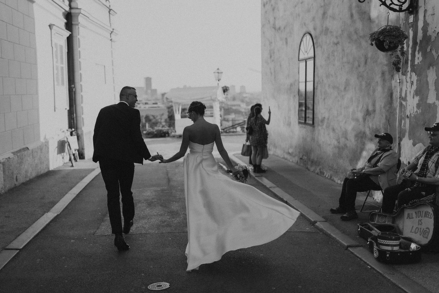 Black and white photo of couple walking down street with bride's dress flowing in motion.