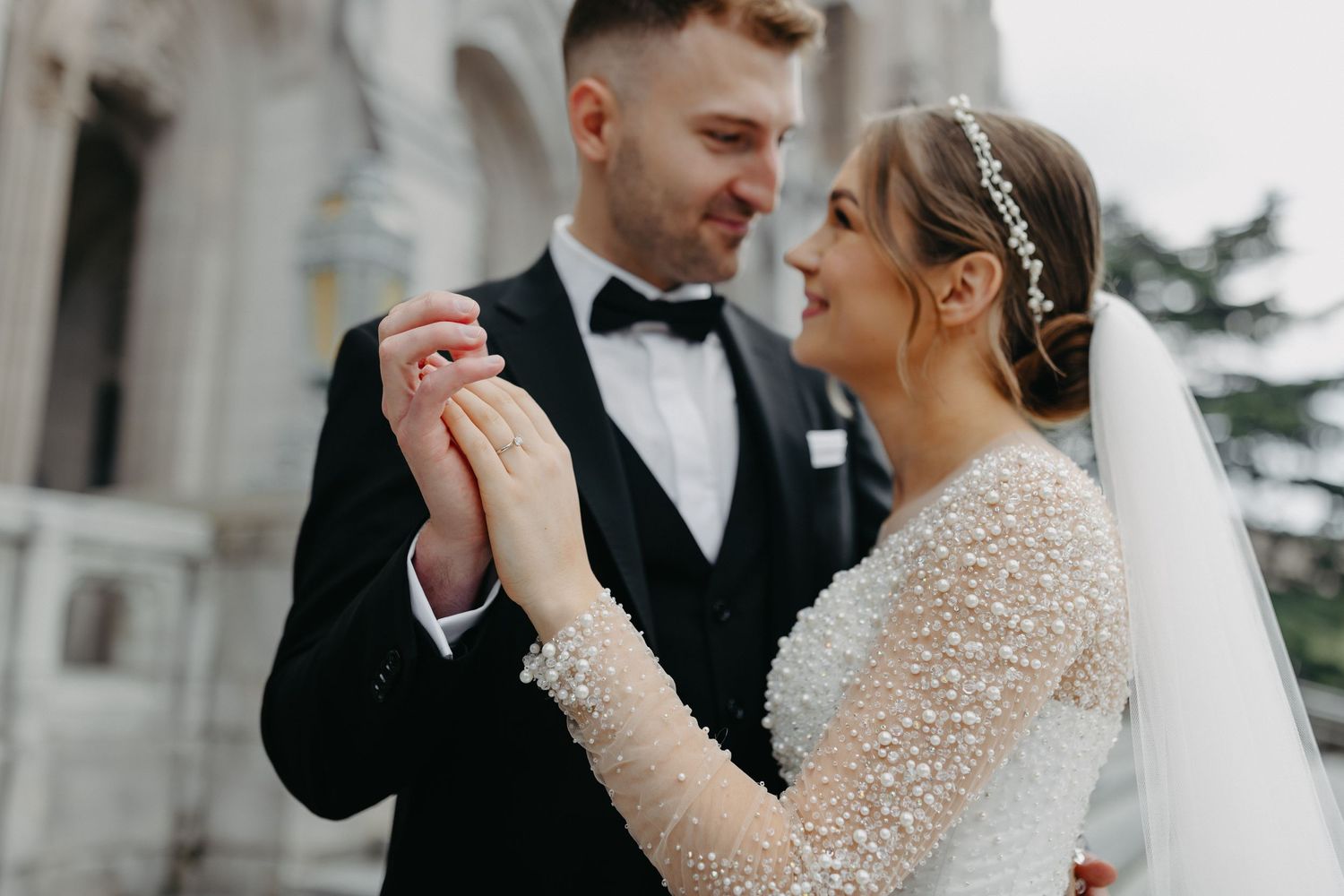 Romantic wedding portrait showing couple holding hands with elegant lace dress and black tuxedo details.