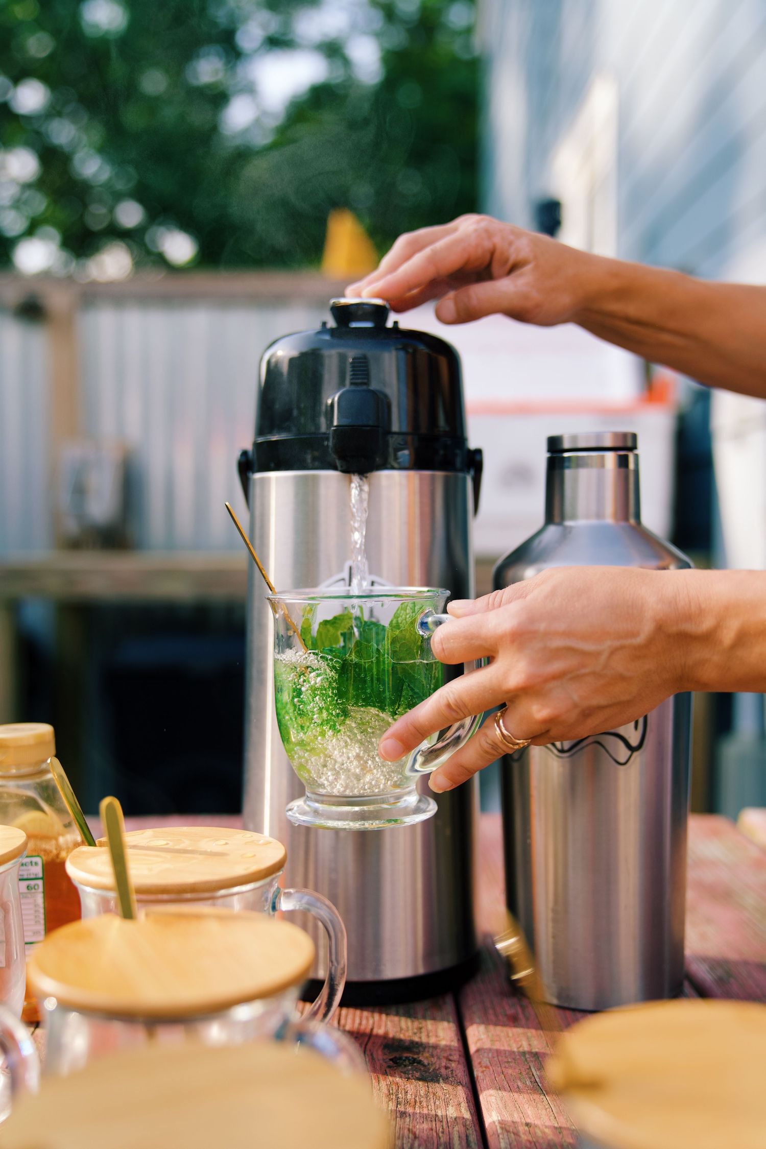 Someone preparing a fresh green drink in a blender on an outdoor wooden table.